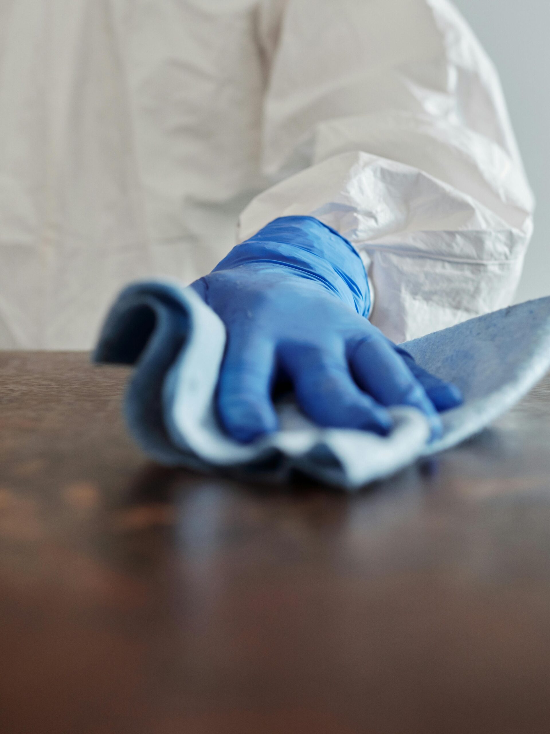 Person in protective suit using disinfectant on surface to ensure cleanliness and safety.